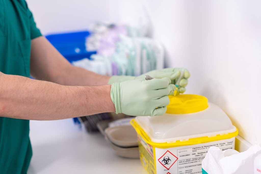 Knights Legal Services - A person in a green scrub suit and green gloves putting something in a container.